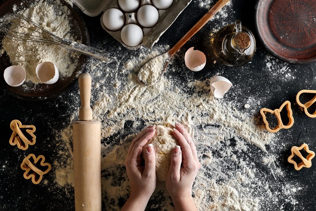 Woman's hands knead dough on table with flour, eggs and ingredients. Top view